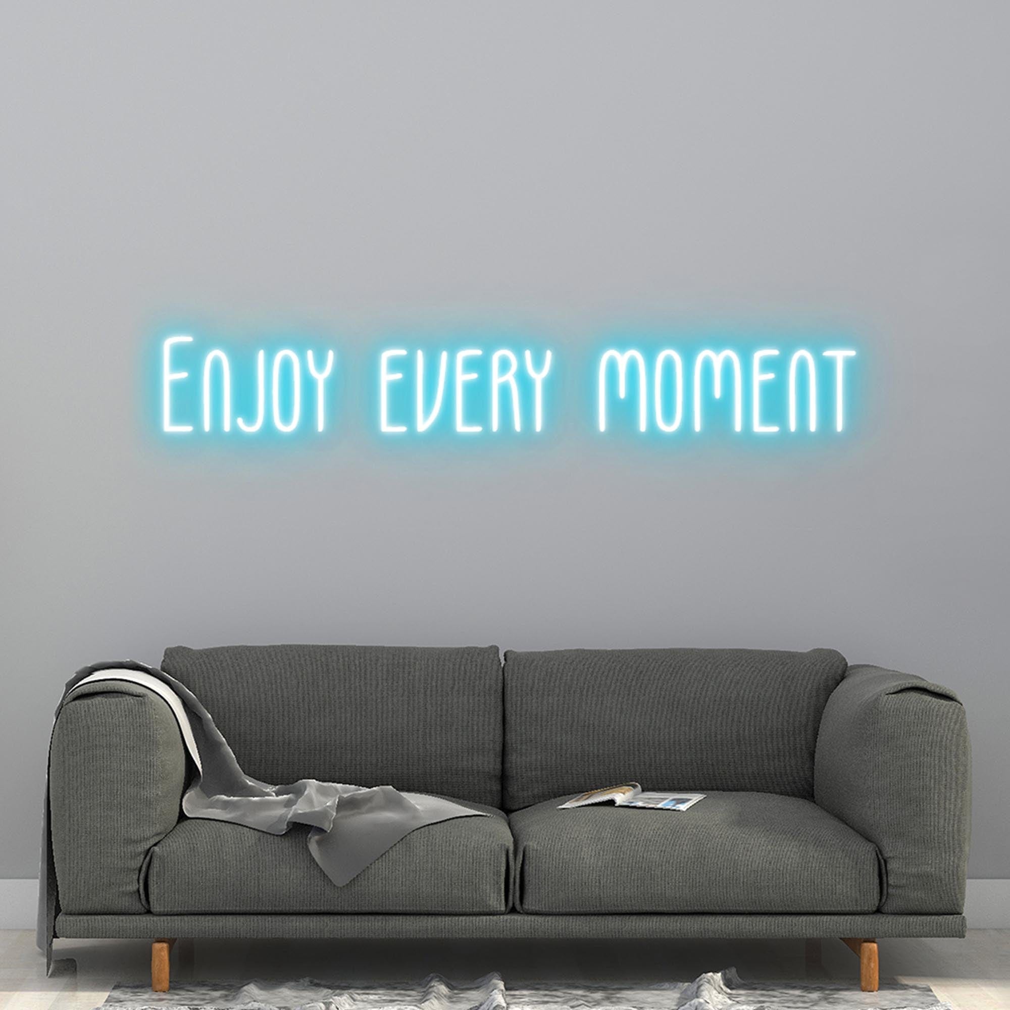 A Iceblue neon sign with the letters "enjoy every moment" is installed on the wall of the living room